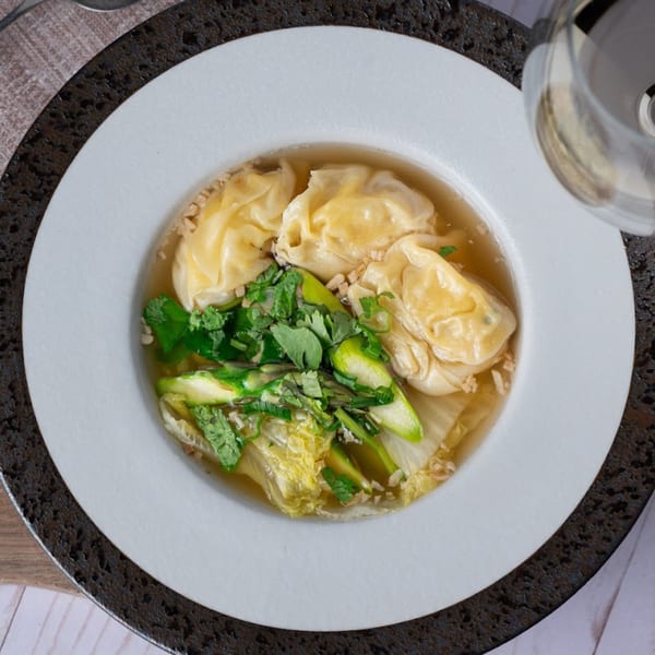 Thai Song's wonton soup with fresh greens, cilantro, and crispy garlic in a white bowl.
