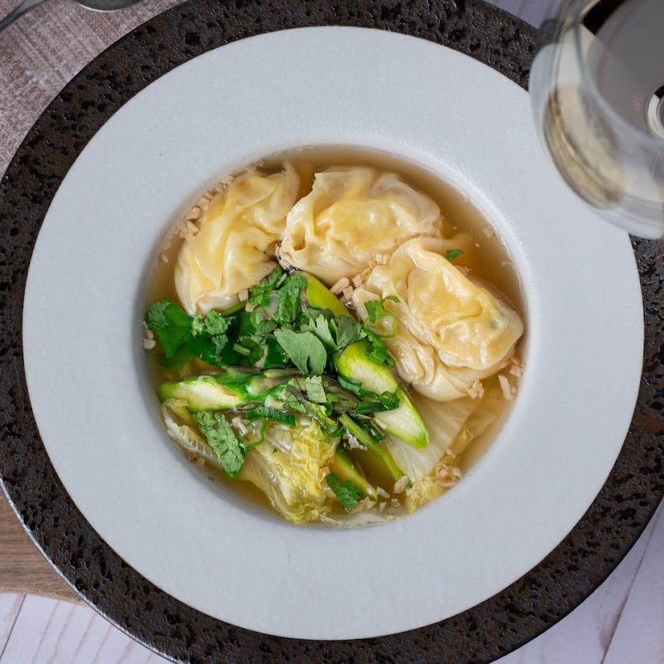 Thai Song's wonton soup with fresh greens, cilantro, and crispy garlic in a white bowl.