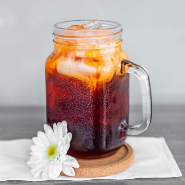 Iced Thai tea in a mason jar mug with a white flower on a coaster and napkin.