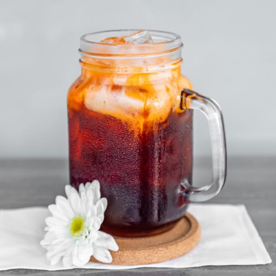 Iced Thai tea in a mason jar mug with a white flower on a coaster and napkin.