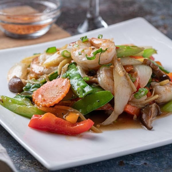 Thai stir-fried shrimp with colorful vegetables like carrots, snap peas, and bell peppers on a white plate.